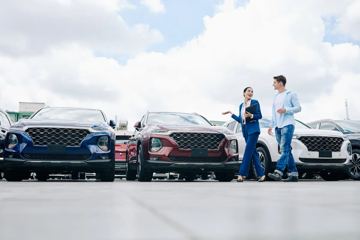 Cheerful saleswoman showing cars to a young man.